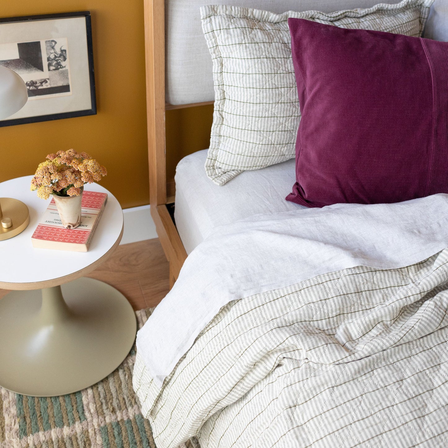 Angled view of Diamond Ticking Quilted Pillow Sham showing green striped diamond quilting on a bed with white linen and a mustard wall background
