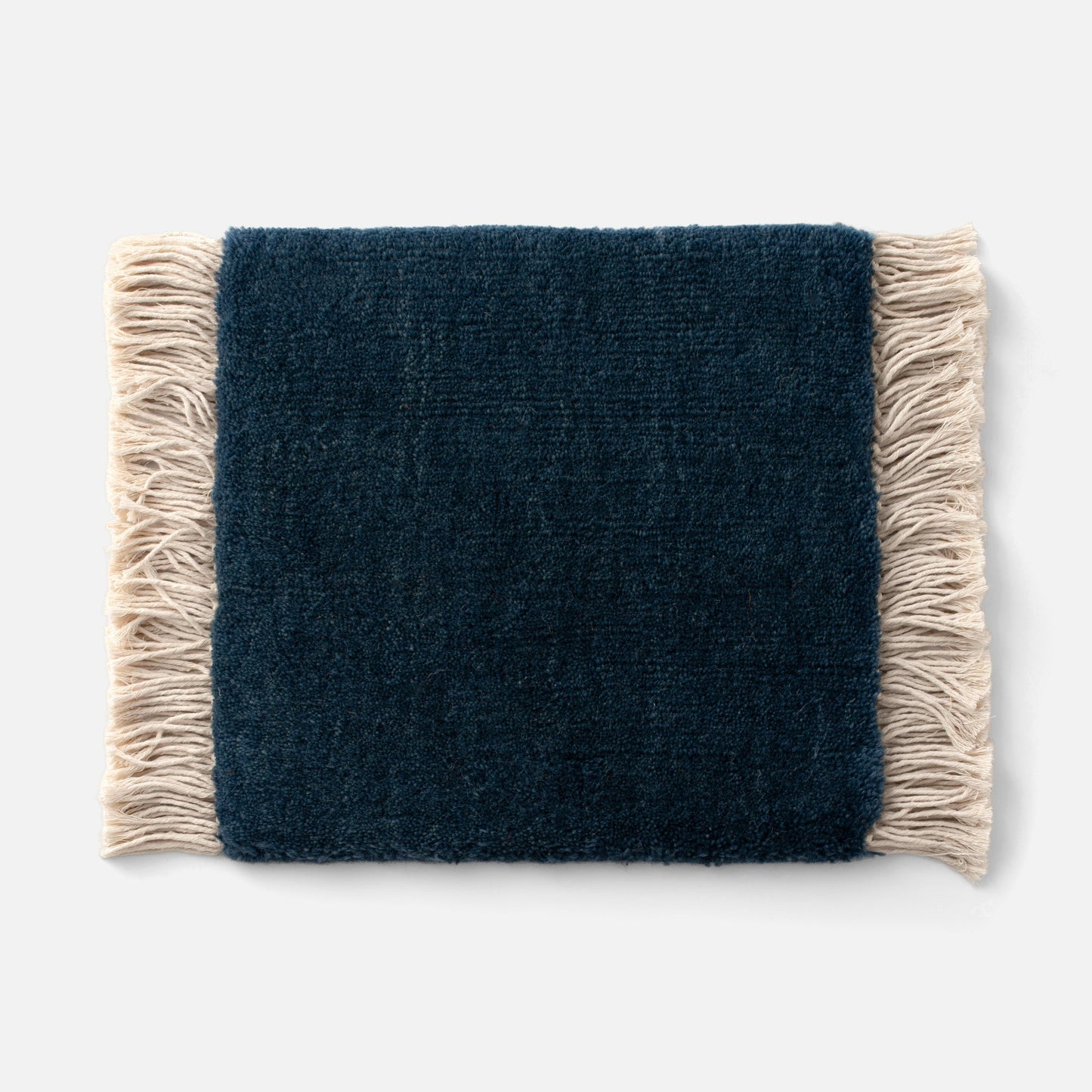 Close-up of Mesa Wool Rug edge showcasing hand-loomed navy wool pile and natural fringe on white background