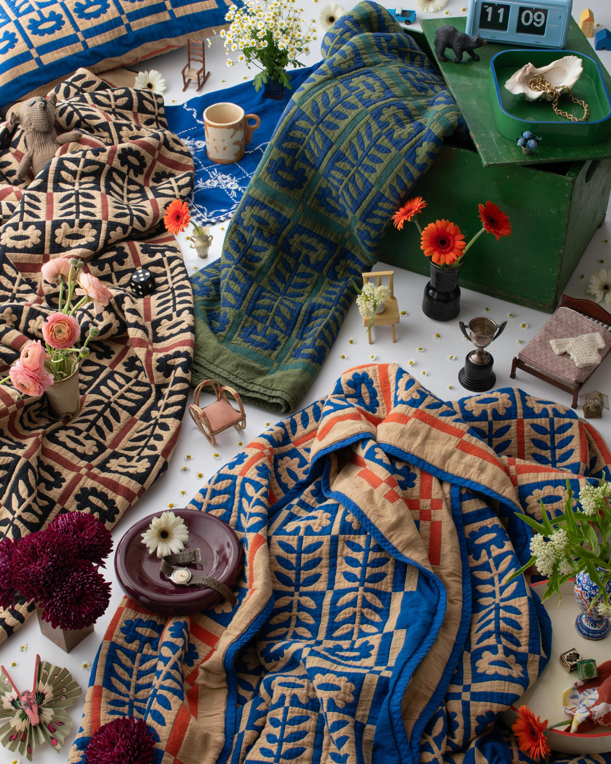 Stillwater quilts arranged with flowers, a mug, toys, and small treasures in a colorful I Spy still life