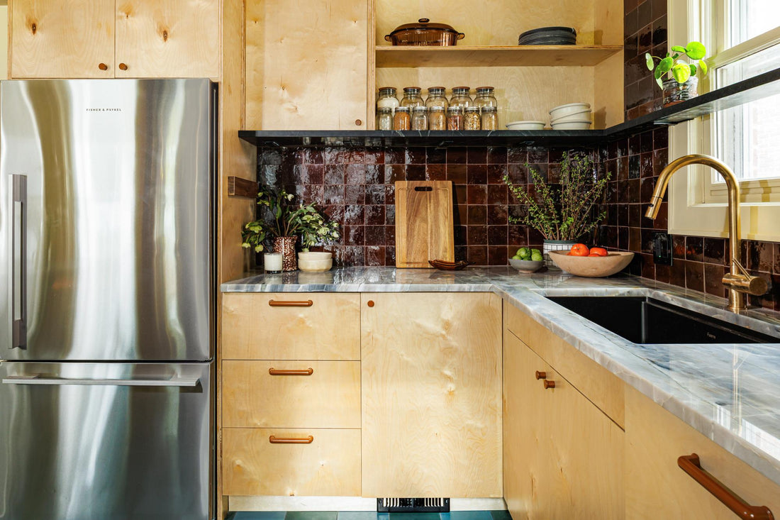 Eclectic kitchen features wood cabinets, dark tile backsplash, marble counters, brass hardware, and a stainless steel refrigerator