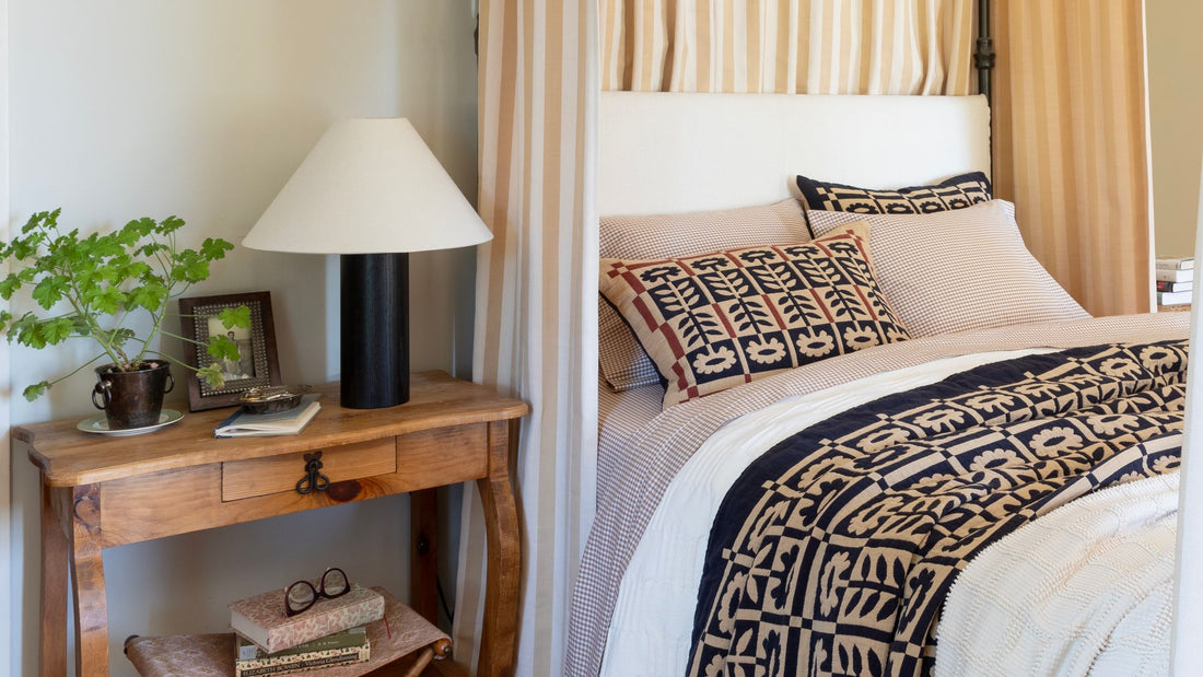 Layered bedroom with a patterned navy and cream bedspread, striped curtains, and a wood console table