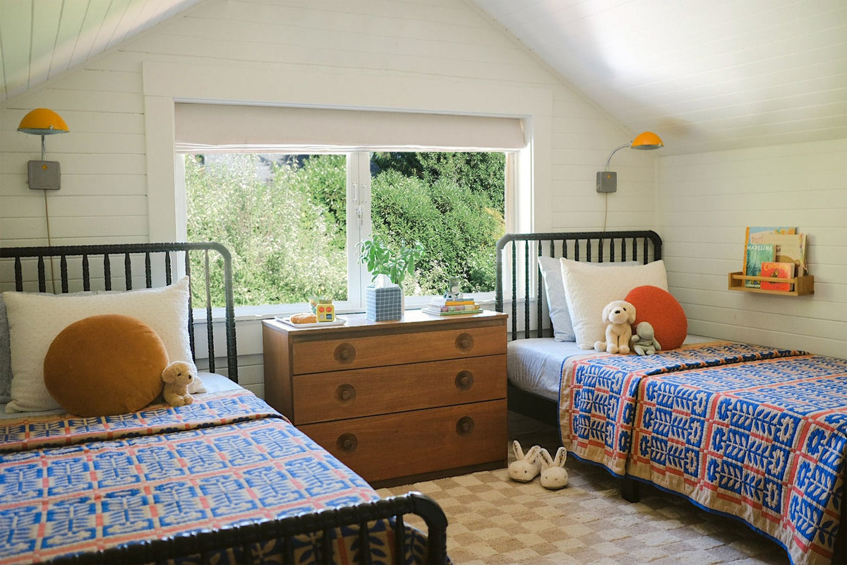 Bedroom with two beds featuring blue, red, and white patterned quilts, black spindle headboards, and a central wooden dresser