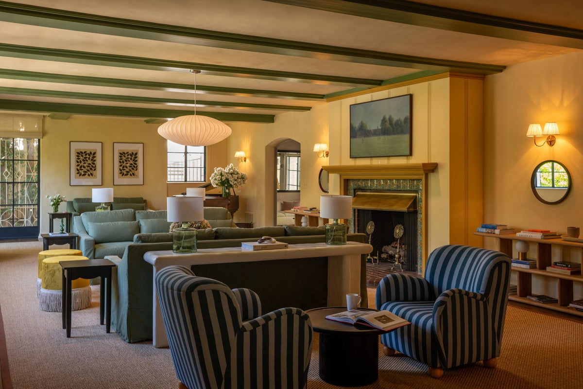 Living room with striped armchairs, green sofas, and a fireplace in a warm yellow interior with green ceiling beams