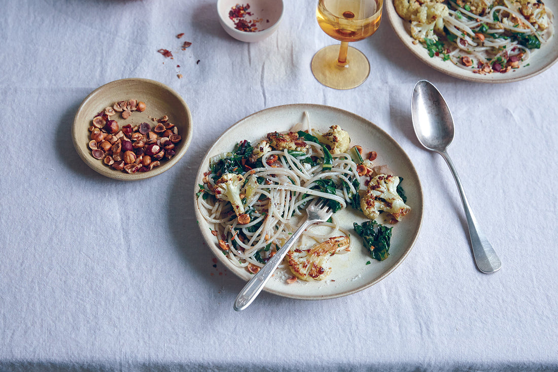 Roasted cauliflower and Swiss chard pasta tossed with chopped hazelnuts, plated overhead on a white linen tablecloth