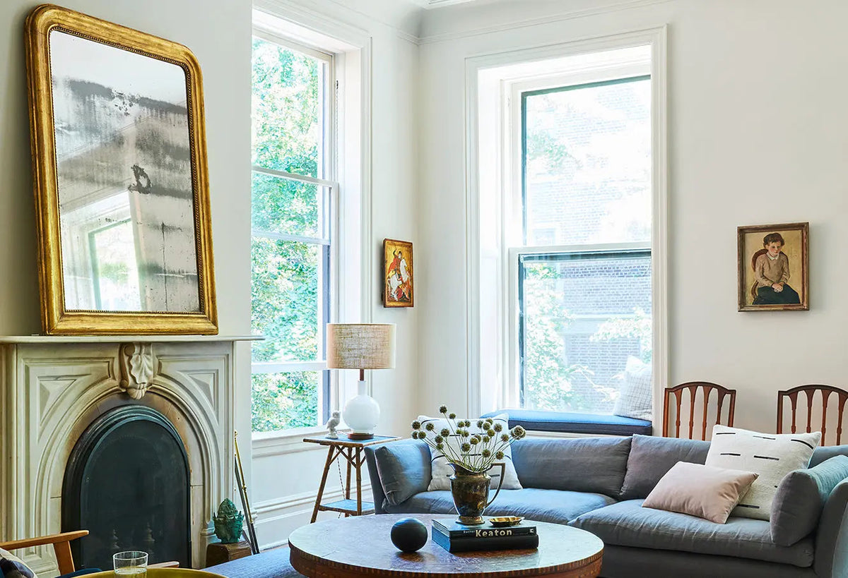 Bright living room with a fireplace, blue sofa, tall windows, and round coffee table