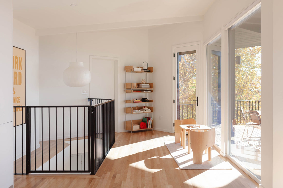 Sunlit landing with black metal railing and small wooden kids’ table and chairs by sliding glass doors to balcony