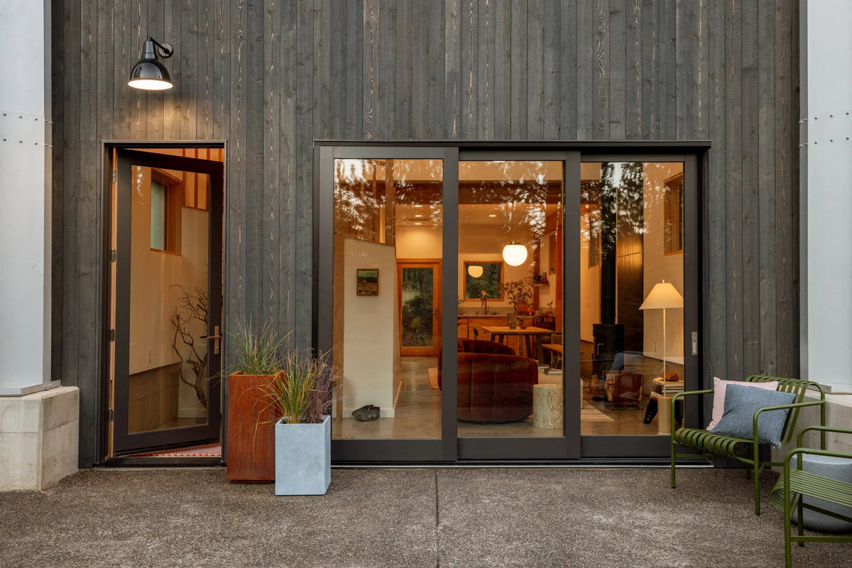 Corrugated steel hut exterior with open door, glass doors, patio chairs, and potted plants