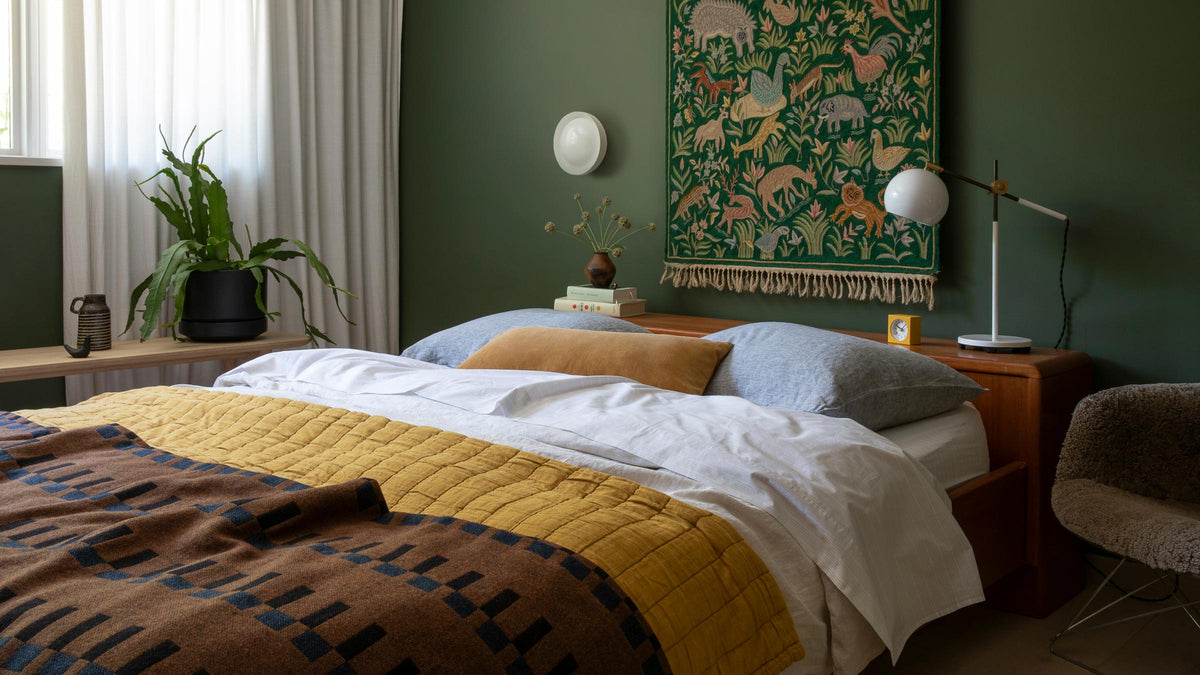 Bed and bedside area featuring a round white wall sconce mounted above a mid-century nightstand against a deep green wall