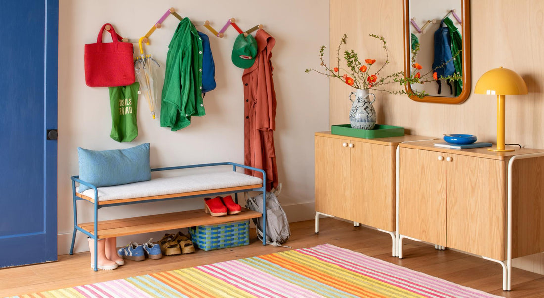 Colorful entryway with a bench, wall hooks, cabinets, mirror, and striped rug