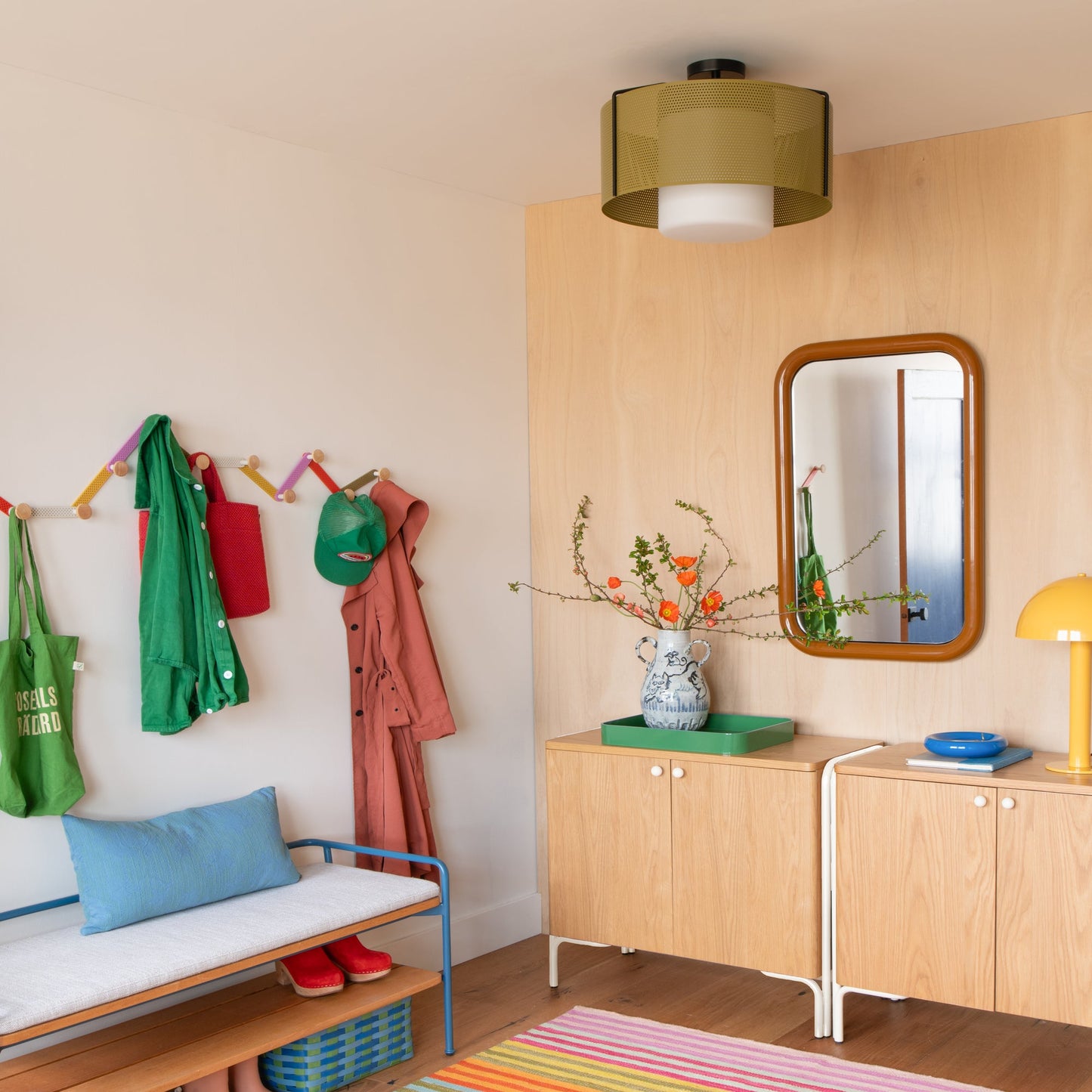 Swell 20-inch flush mount ceiling light with perforated olive metal shade and frosted glass diffuser installed in an entryway with a wood cabinet, mirror, and colorful hooks