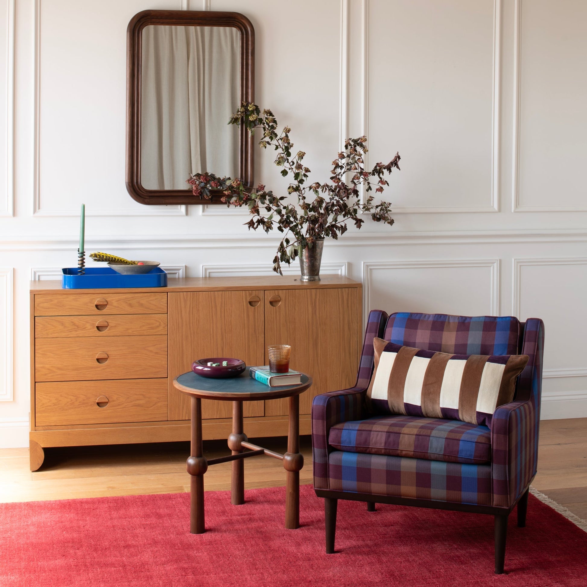 Ann occasional table beside a plaid armchair on a red rug in a paneled living room, styled with a book and glass