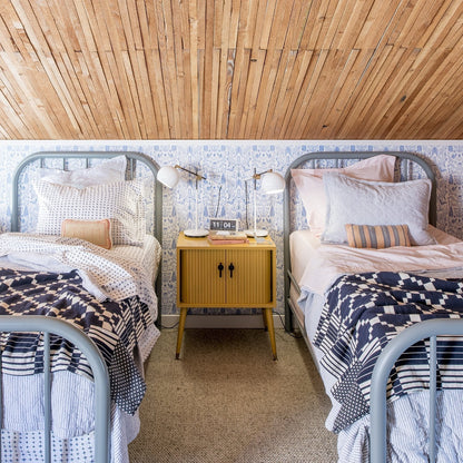 Two twin beds styled with Diamond Ticking Quilted Pillow Shams on patterned bedding in a bright kids’ bedroom with wood-plank ceiling and yellow nightstand