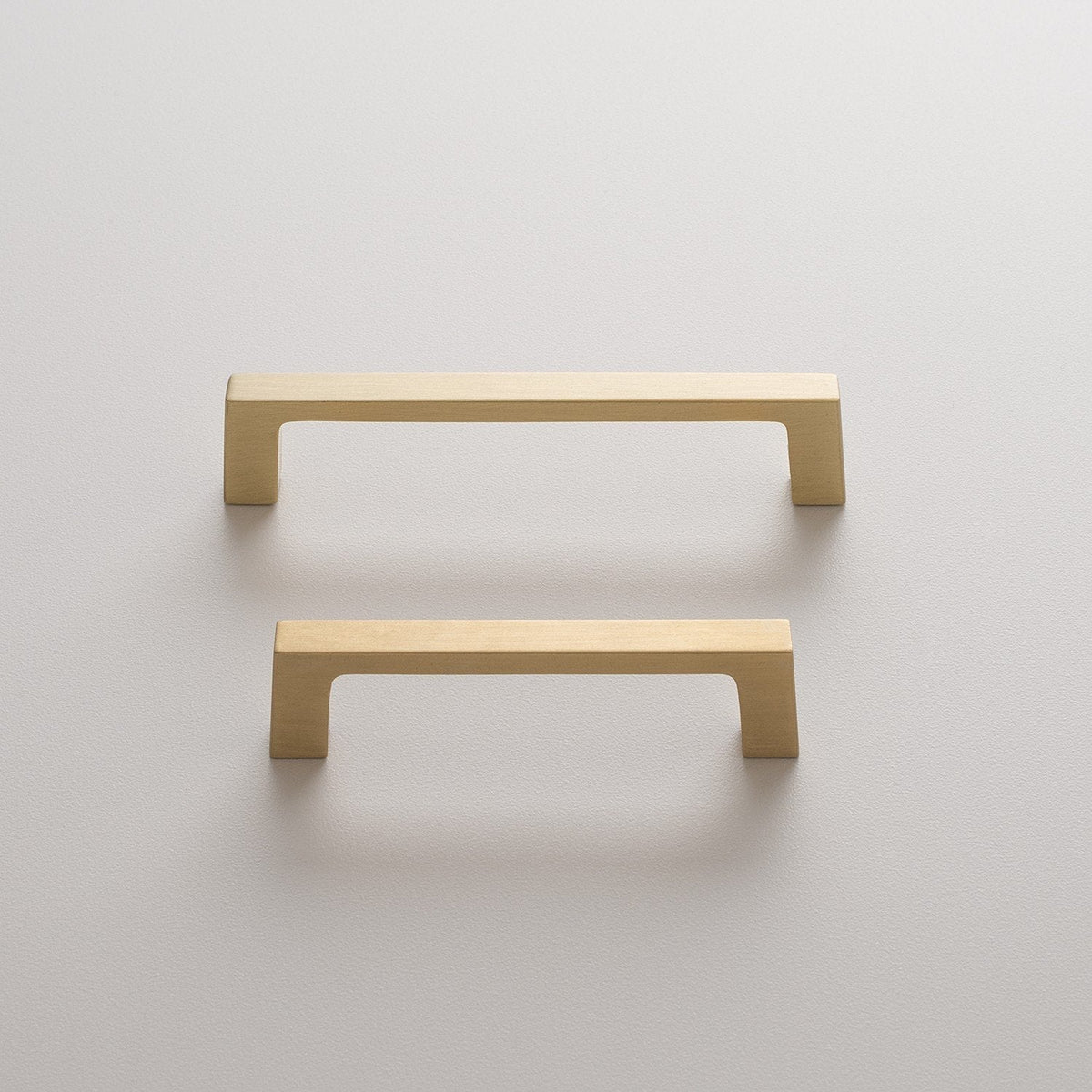 Front view of two Greenwood Pull drawer pulls in natural brass showcasing thin profiles and splayed stems against a light wall