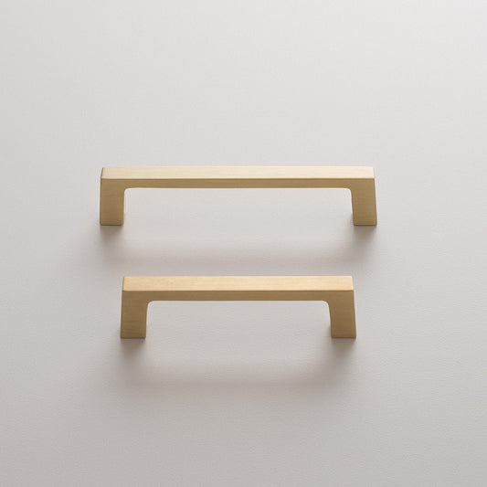 Front view of two Greenwood Pull drawer pulls in natural brass showcasing thin profiles and splayed stems against a light wall