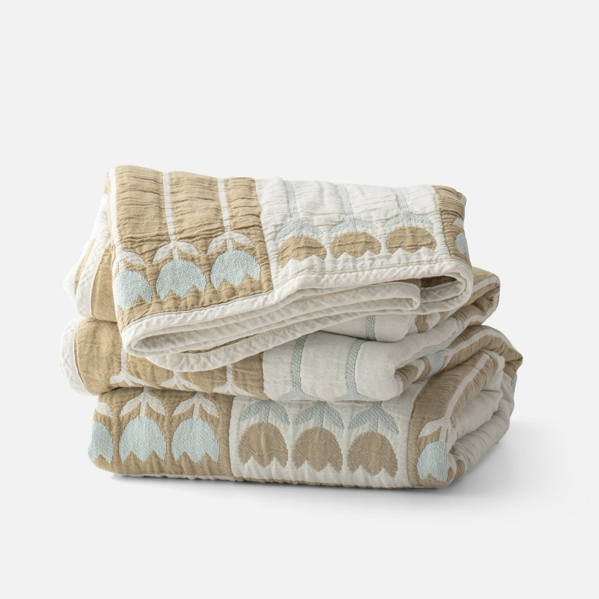 Folded view of the Tulbend Quilt showcasing tan and light blue arch pattern with a white background