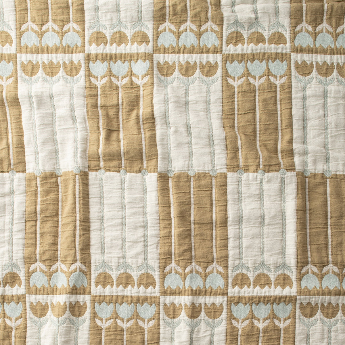 Close-up of Tulbend Quilt showcasing stitched tan, cream, and pale blue tulip patterns