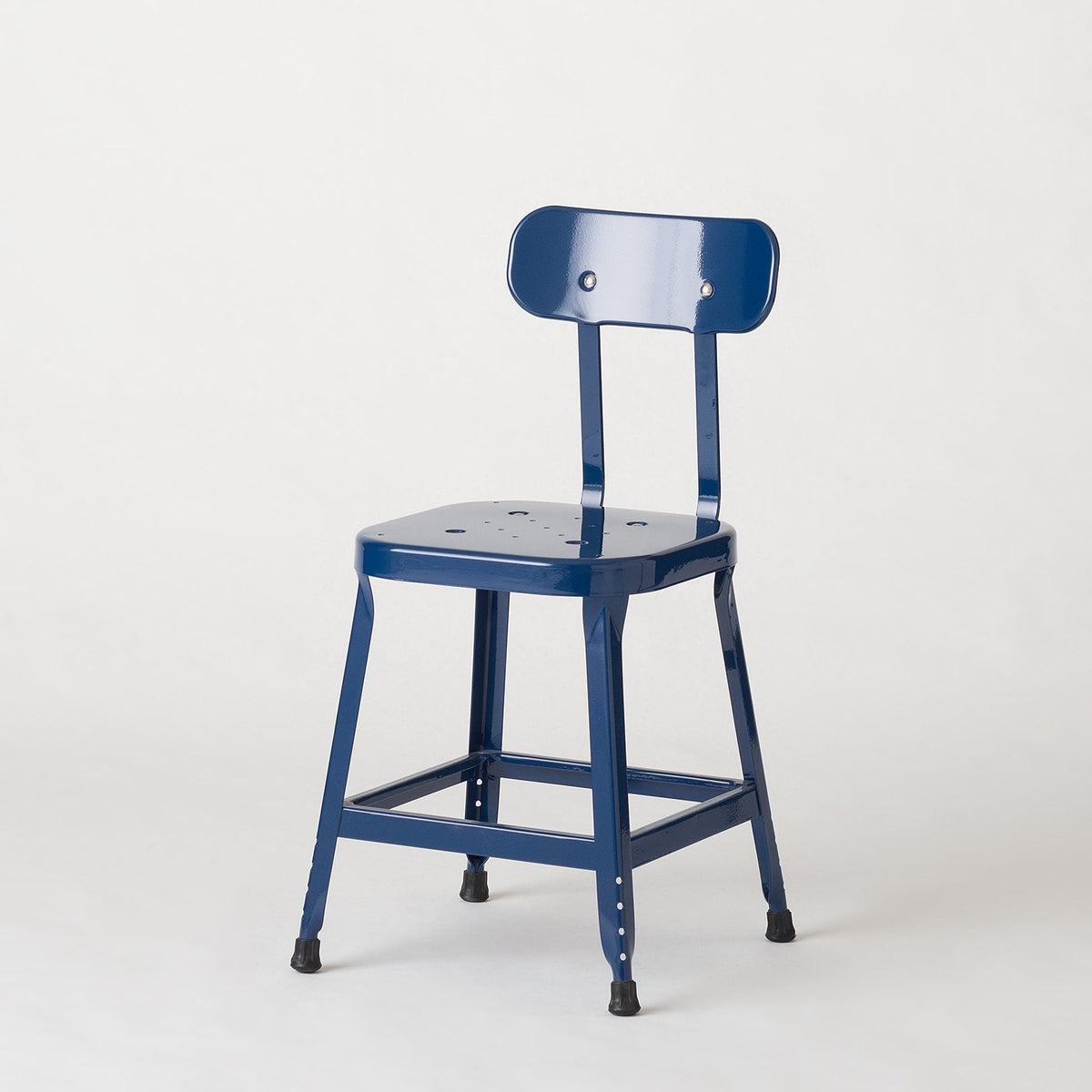 Three-quarter view of Schoolhouse Utility Stool in indigo gloss, showing stamped steel seat and rubber feet on white background