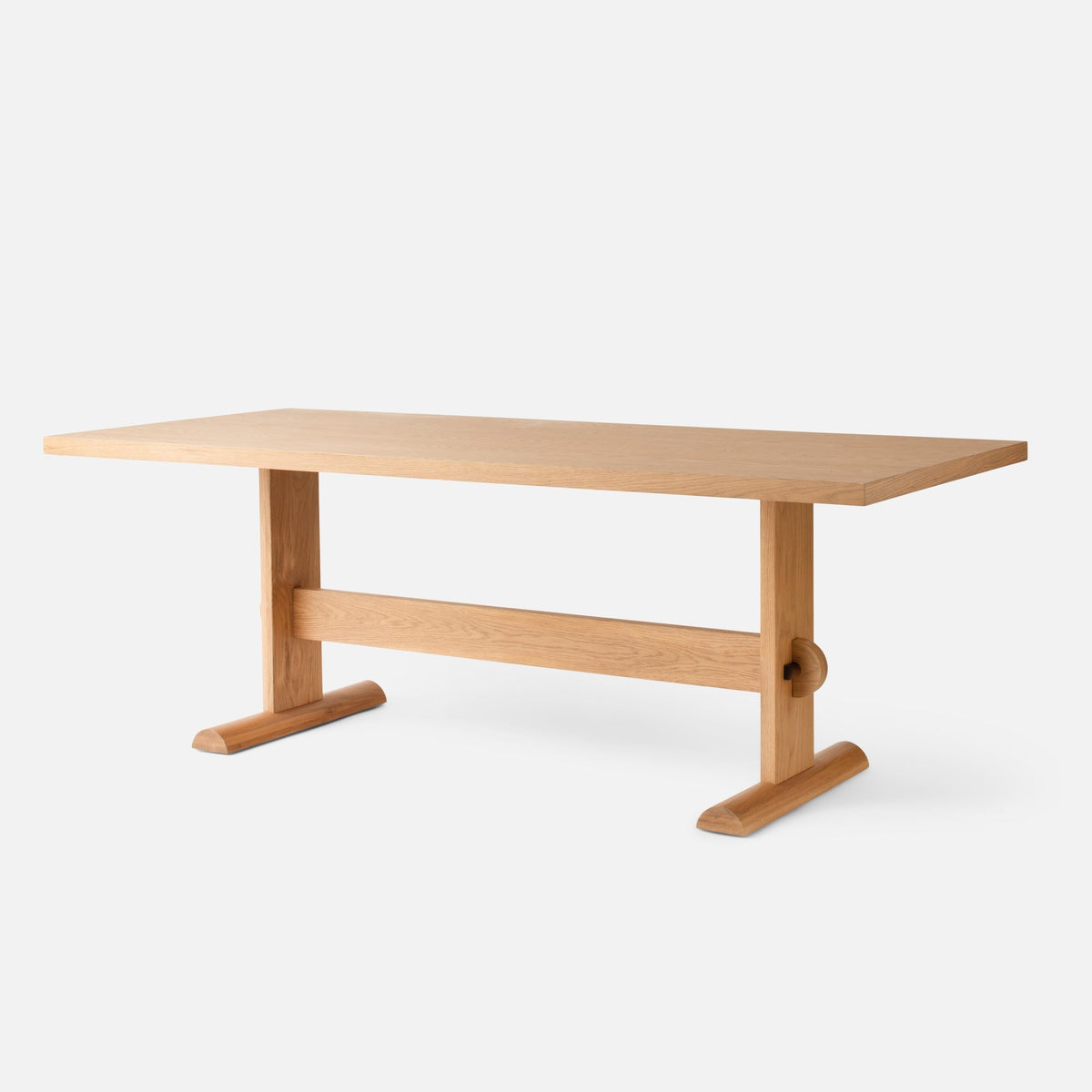 Front three-quarter view of Darrow Dining Table showcasing an oak top, trestle legs, and stretcher on a light gray background