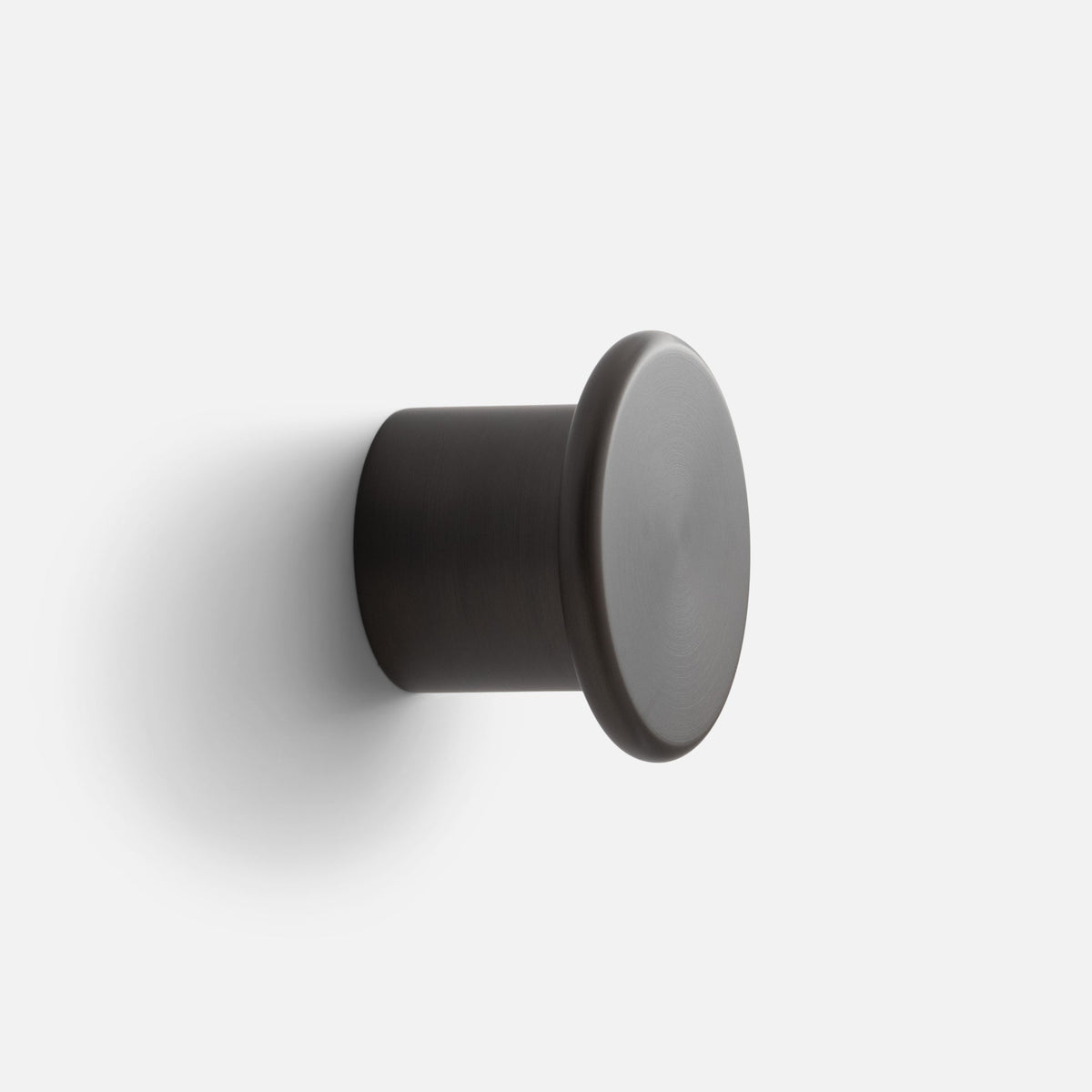 Close-up side view of Remy Single Hook showcasing its cylindrical form and rounded face against a white wall