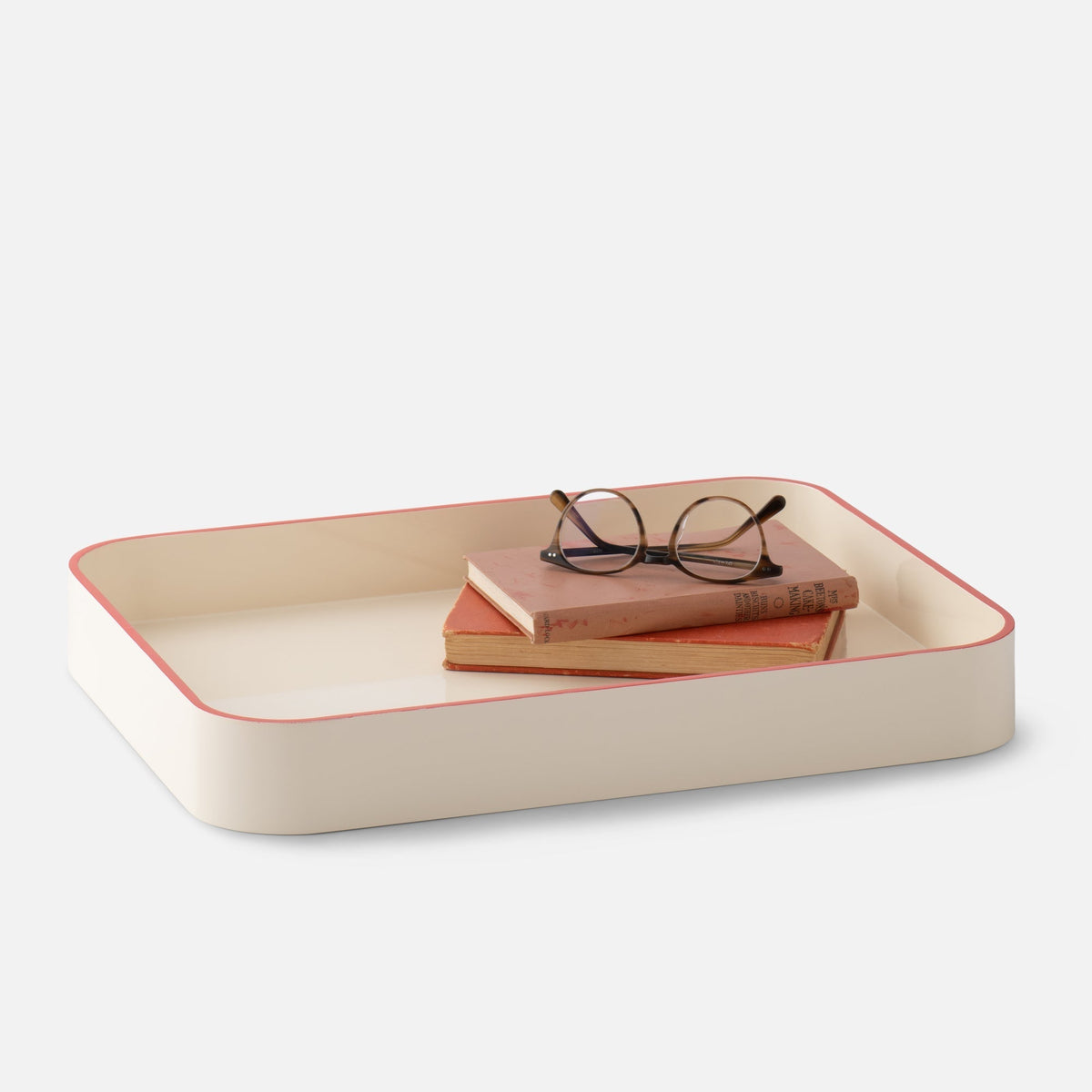 Three-quarter view of Clare V Sonia Tray showcasing rounded corners and pink trim with books and glasses on white background
