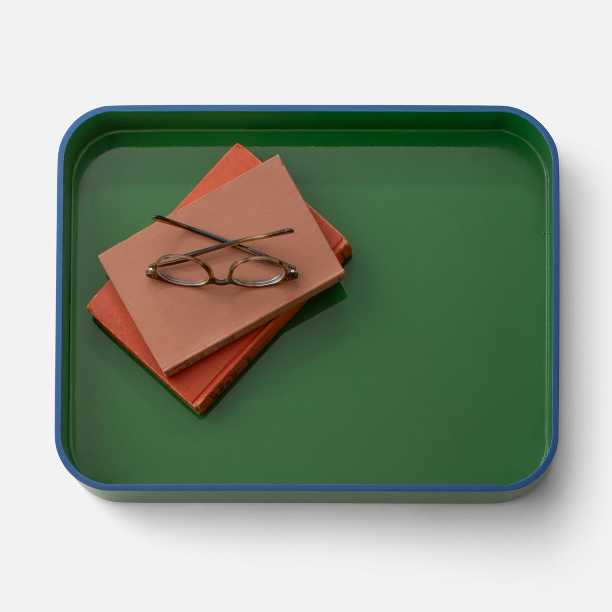 Top view of Clare V Sonia Tray showcasing its green surface and blue rim with books and eyeglasses on a white background