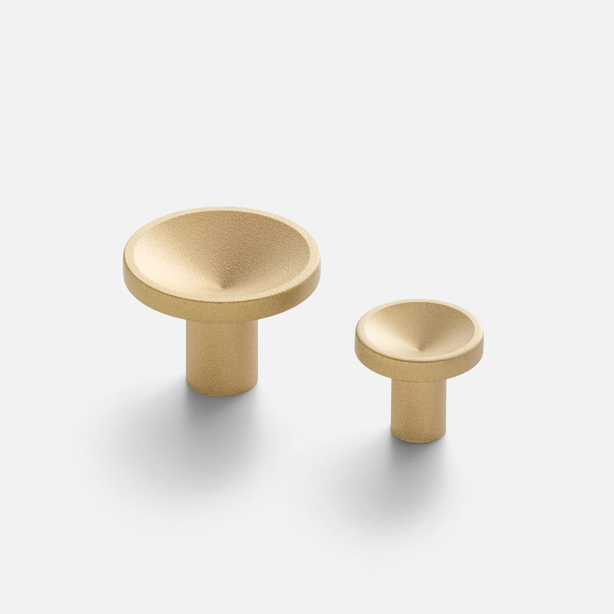 Angled view of two Rhone Cast Brass Knobs showcasing minimalist textured shapes on a white background
