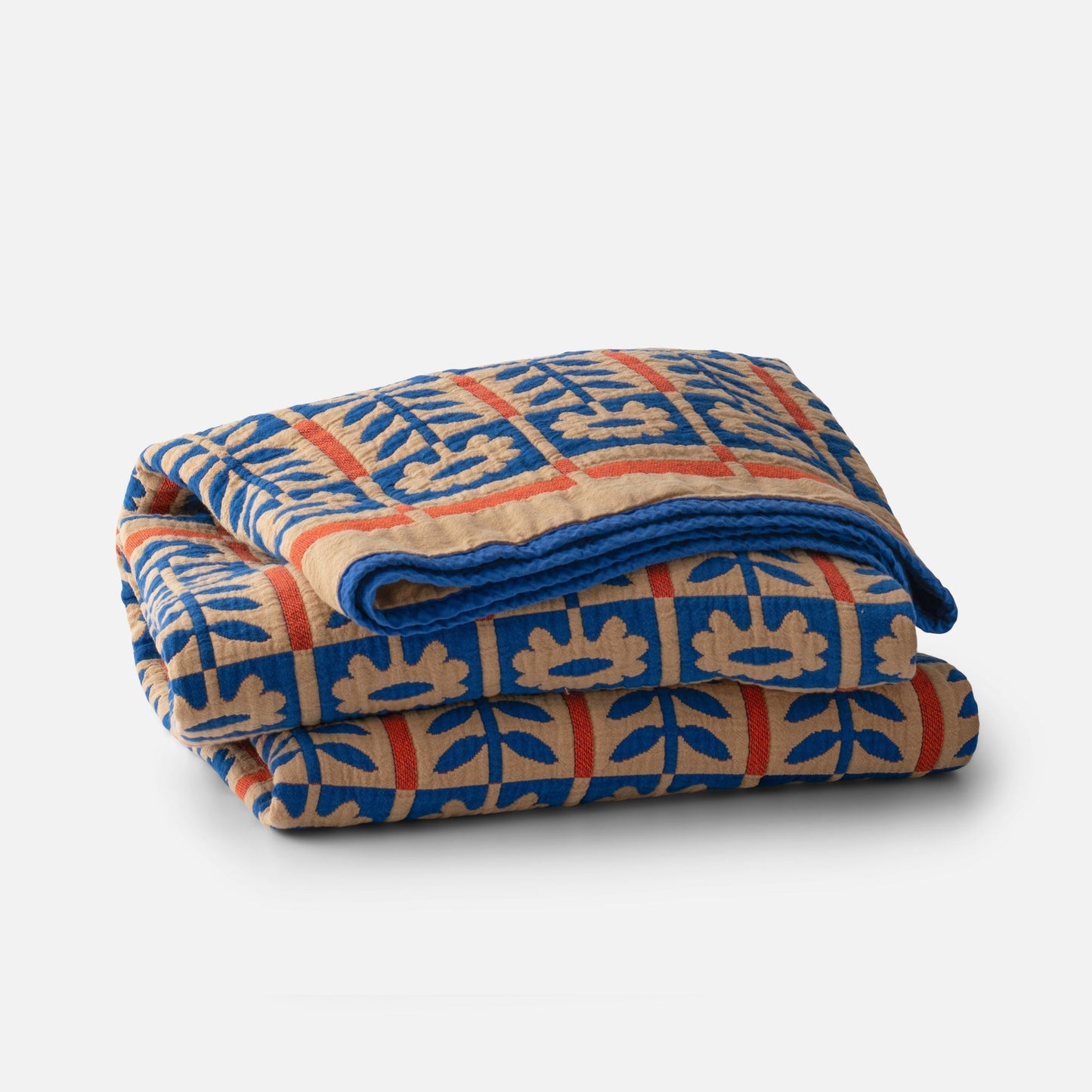 Close up of folded Stillwater Floral Quilt showing blue, tan and orange jacquard floral pattern on white background
