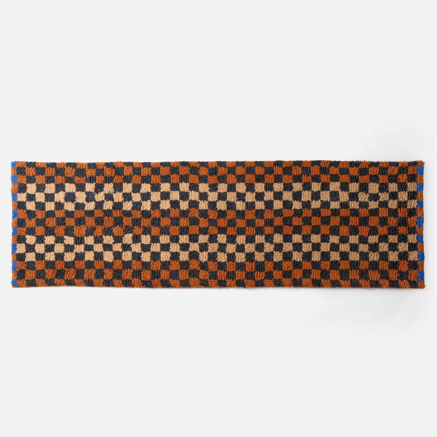 Top edge view of Felix shag wool rug showcasing butterscotch and navy checkerboard pattern and high-pile texture on white background