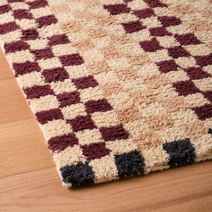 Close-up angled view of Schoolhouse x Clare V Felix shag wool rug showing high-pile handloomed wool and contrasting checker pattern on a wood floor
