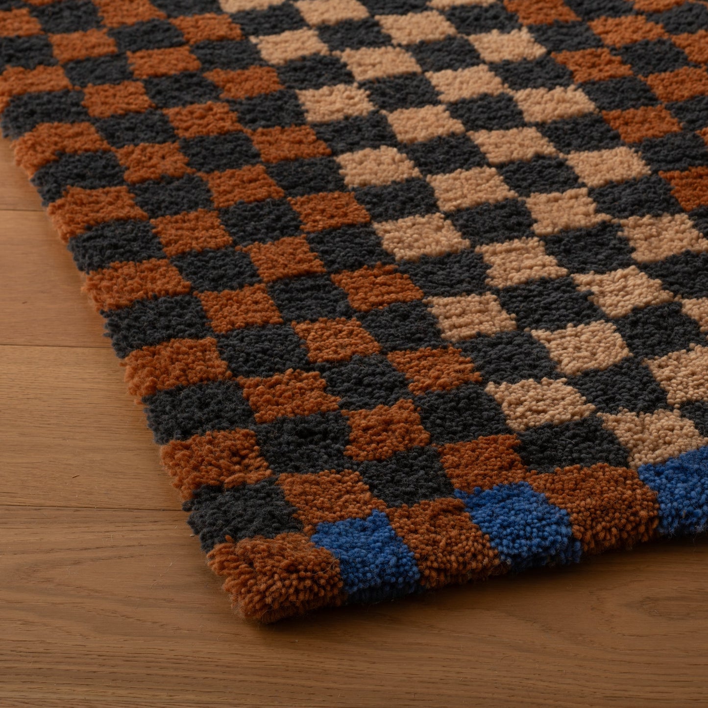 Angled close-up of Felix shag wool rug showcasing high pile checkerboard pattern in butterscotch, charcoal, and tan on a wood floor