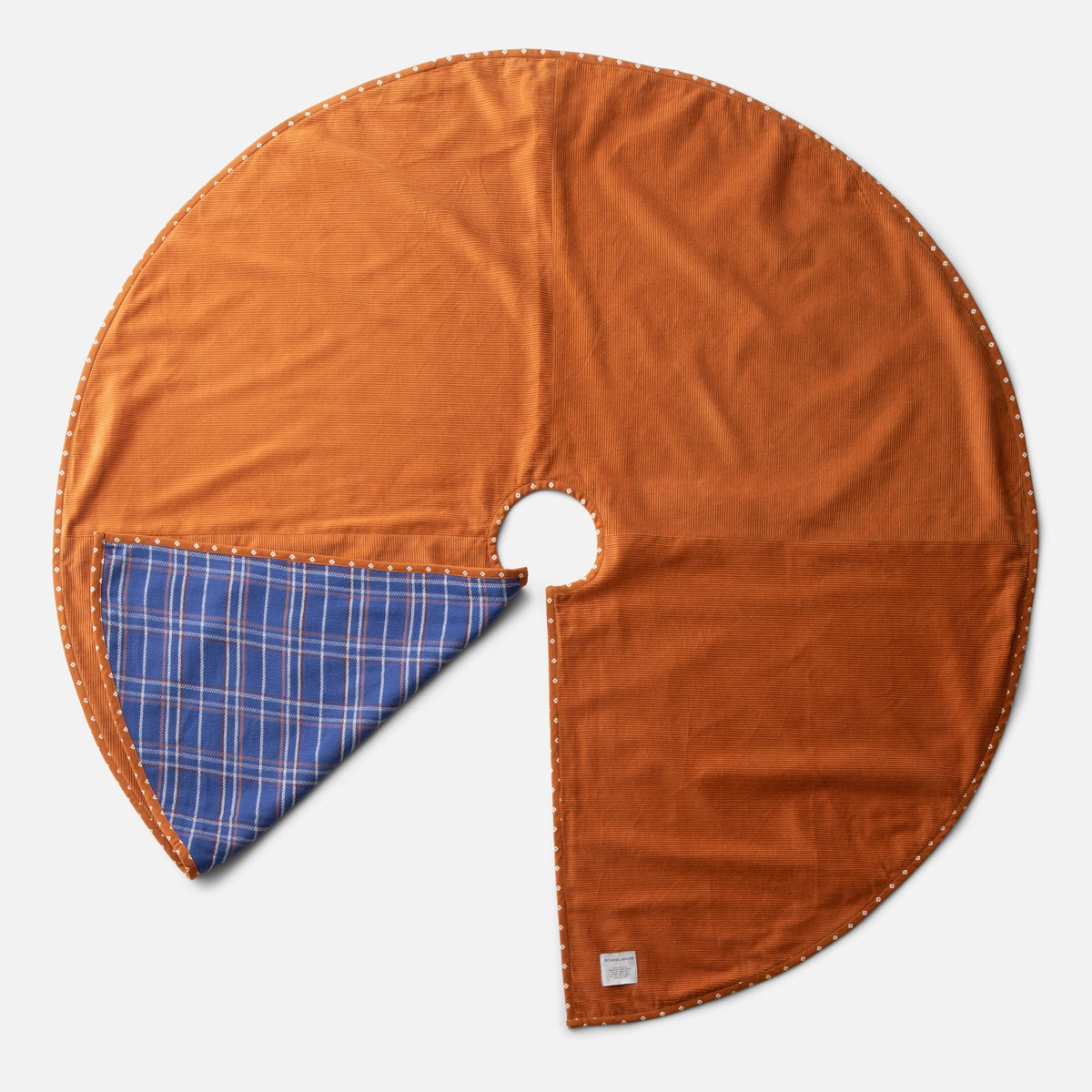 Top view of Haberdasher’s Tree Skirt showcasing rust corduroy, blue plaid, and patterned trim with a light gray background