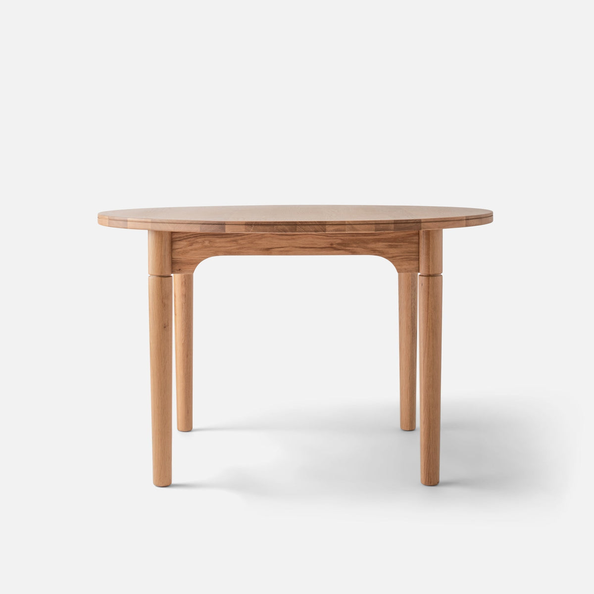 Front view of Willard Dining Table showcasing softly rounded oak tabletop and tapered legs with a white background