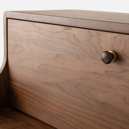 Close-up view of Peggy Cabinet showcasing its wood-grain front and round drawer knob with a light background