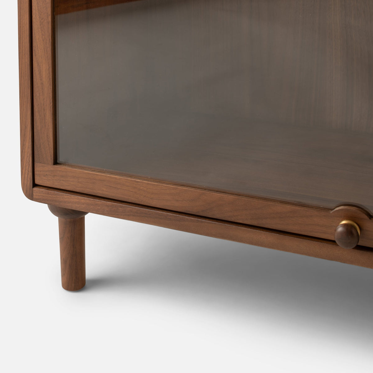 Close-up view of Peggy Cabinet showcasing wood framing, glass door, rounded leg, and round knob against a white background
