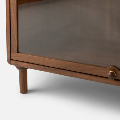 Close-up view of Peggy Cabinet showcasing wood framing, glass door, rounded leg, and round knob against a white background