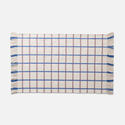 Flat-lay of Cotton Grid Flatweave Rug showcasing blue and brown large grid pattern and fringed ends on a white background