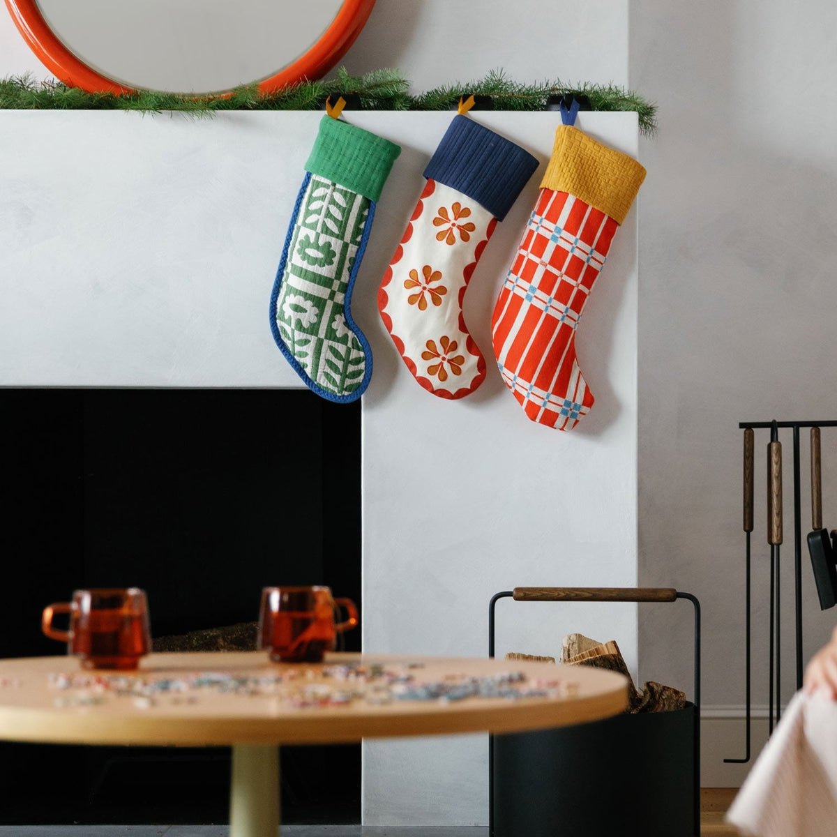 Shelburne stocking hangs with two patterned stockings above a fireplace in a living room