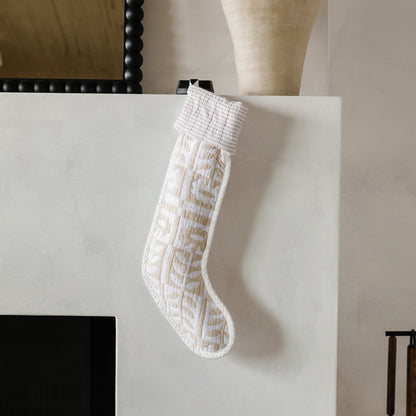 Front view of Stillwater Stocking showcasing its quilted floral pattern and striped cuff with a white fireplace background