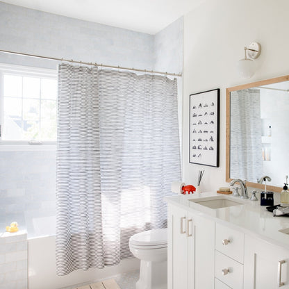 Striped shower curtain in a bright white bathroom with a bathtub, toilet, vanity, and mirror
