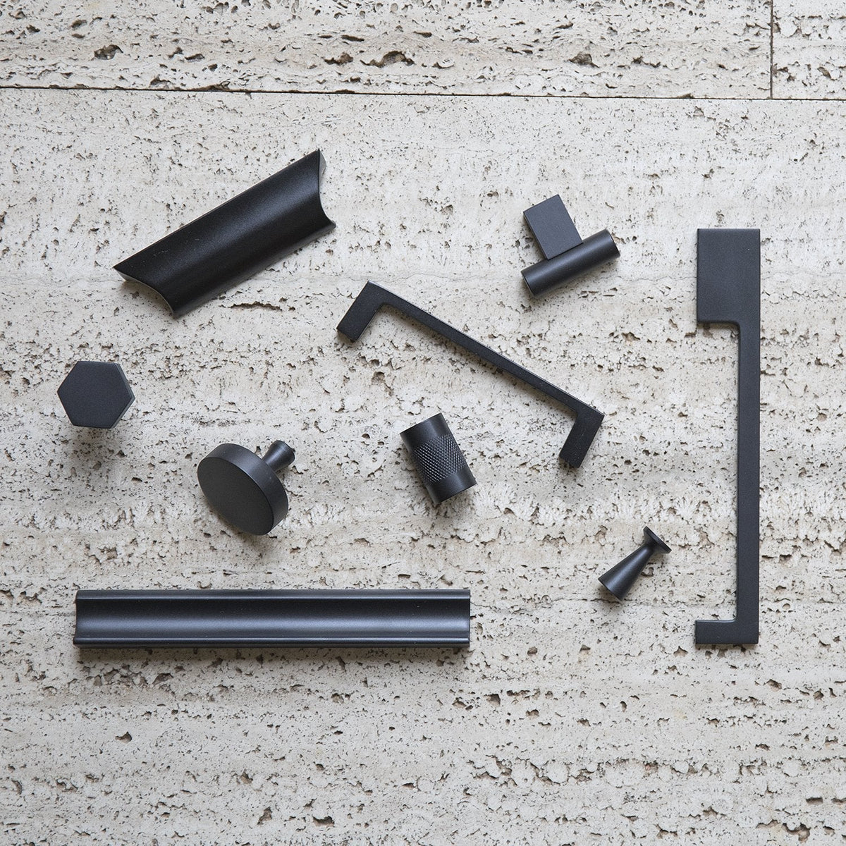 Top view of Alberta Pull showcasing its thin asymmetrical profile among black hardware on a textured stone surface