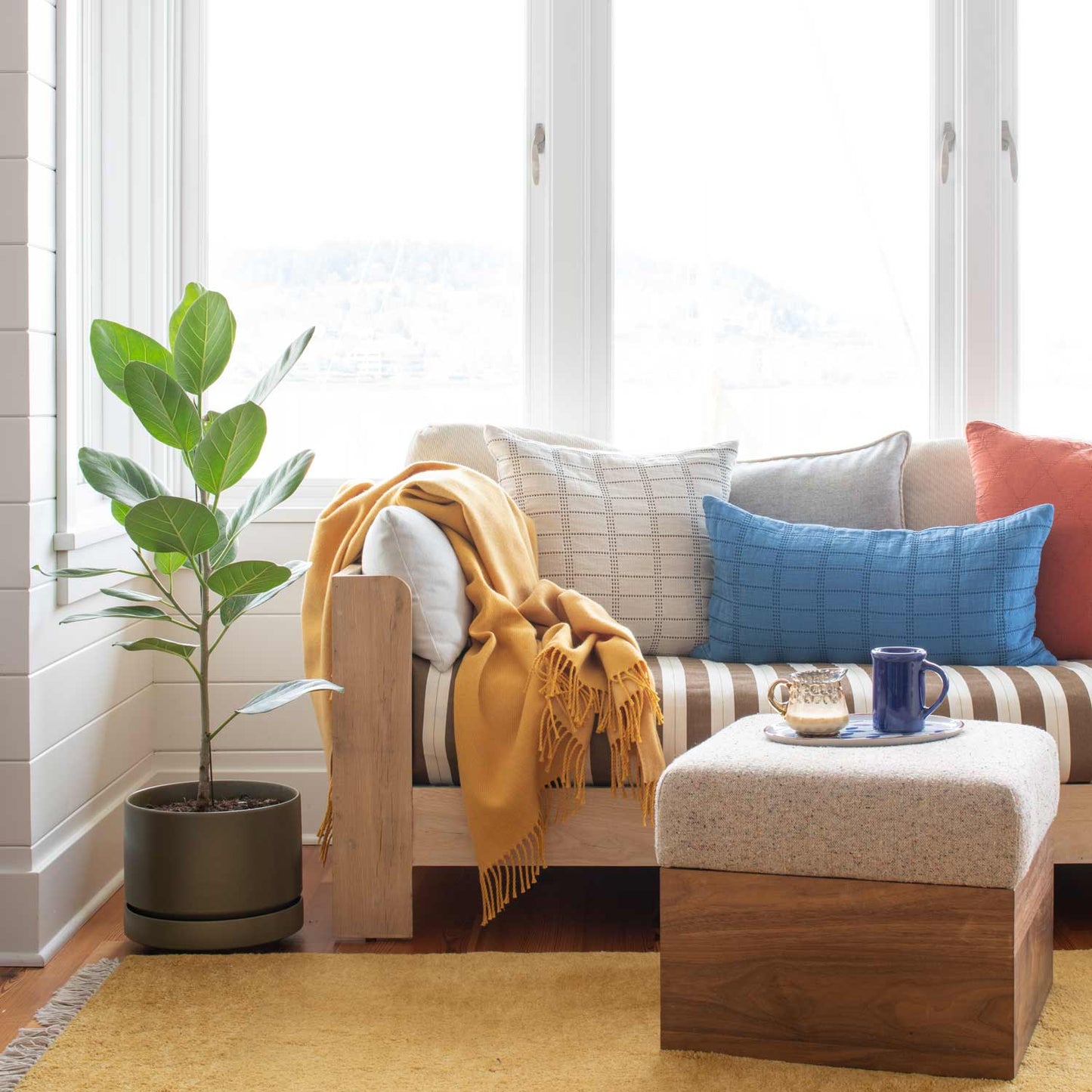 Sunlit corner showing Mesa Wool Rug under a wooden daybed with striped cushions, mustard throw, and potted fiddle leaf fig