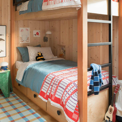 Shelburne Coverlet drapes over a bed in a wood-paneled bunk room with blue and red plaid bedding