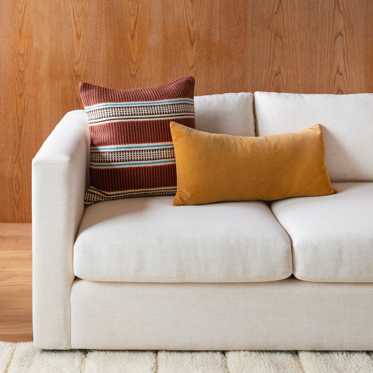 Striped Anders pillow cover styled on a white sofa with a mustard cushion and wood-paneled wall