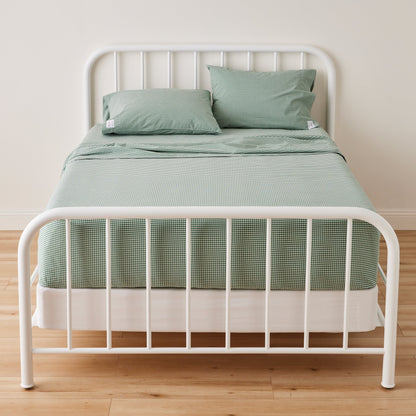 Front view of Gingham Pillowcase showcasing a green gingham pattern on a bed with a white metal frame