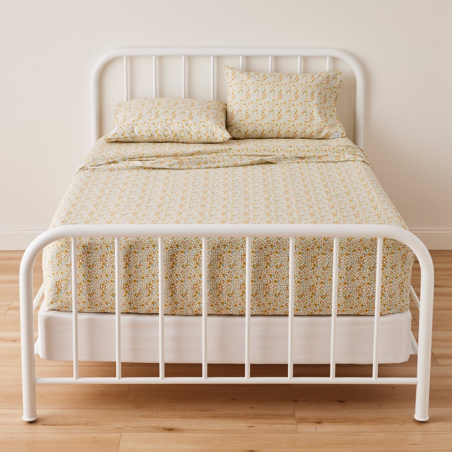 Front view of Wallowa Floral Percale Sheet Set showing small yellow floral print on 100% cotton percale on a white metal bed frame