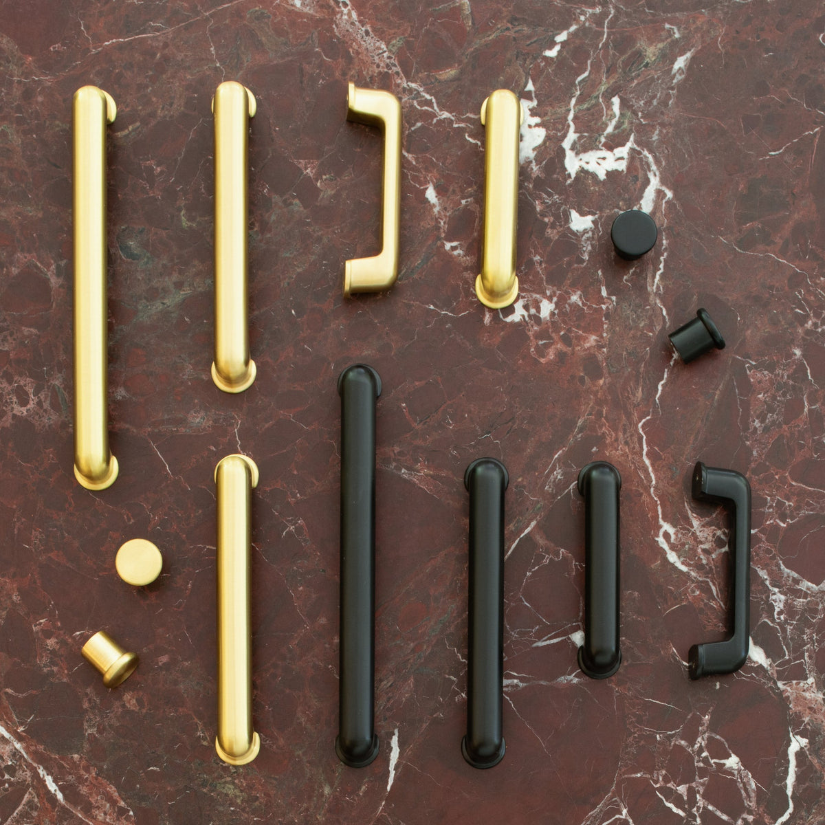 Overhead view of the Remy Knob in solid brass among assorted pulls on a red marble surface