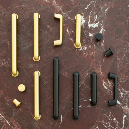 Overhead view of the Remy Knob in solid brass among assorted pulls on a red marble surface