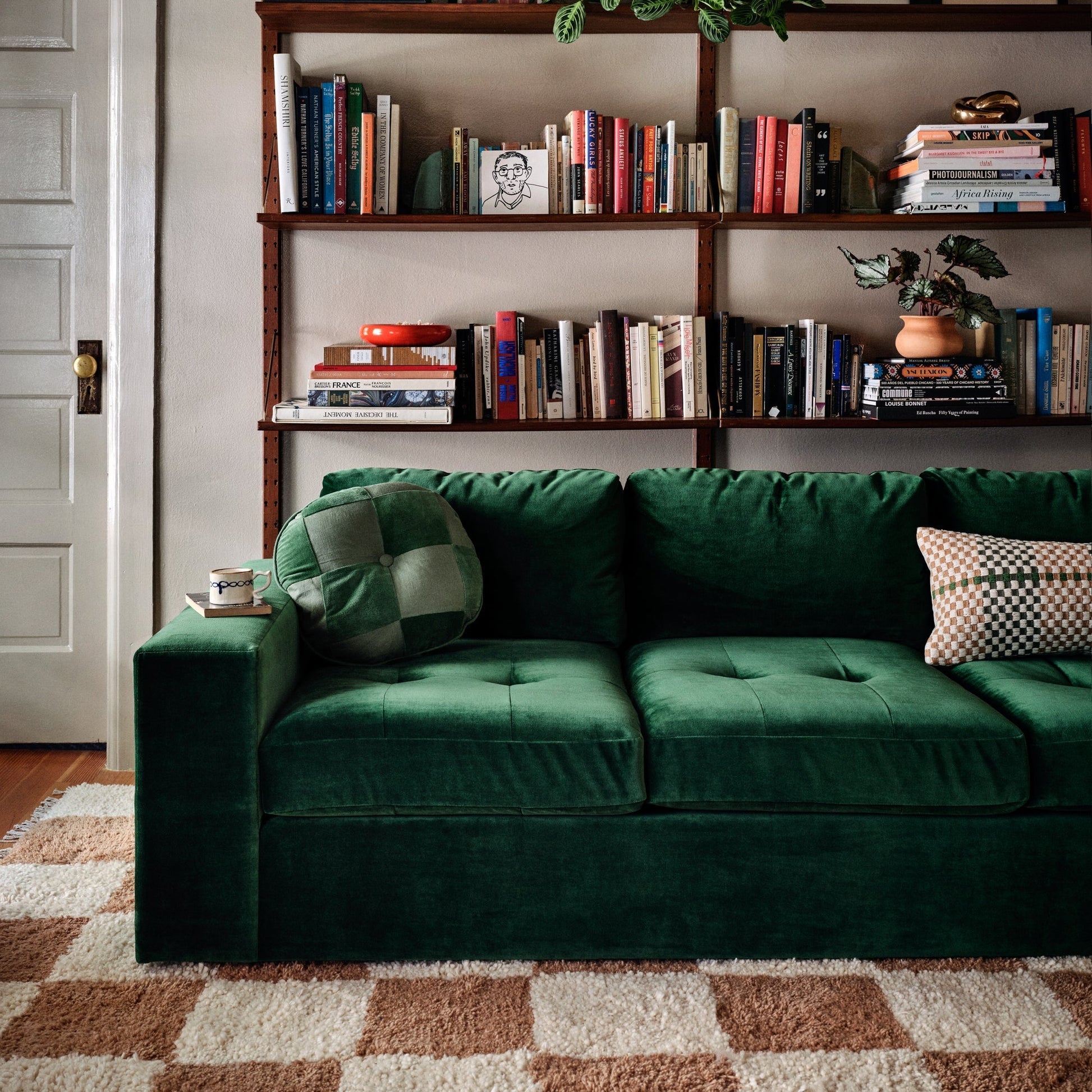 Cream and brown checkered high-pile shag rug under a green velvet sofa in a cozy living room with wooden bookshelves