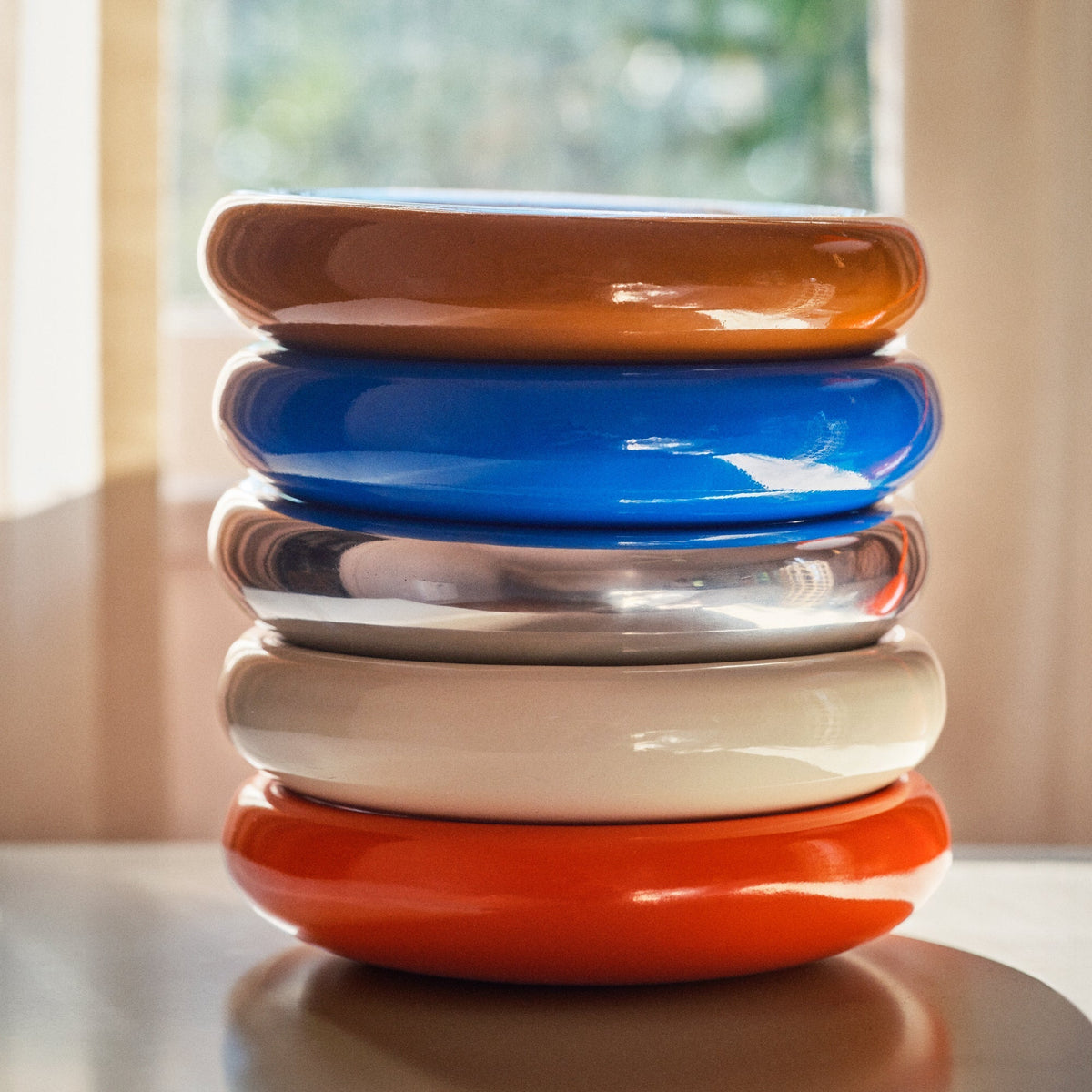 Stacked view of five Schoolhouse x Clare V. Yves Cast Metal Catch Alls showcasing bold colors with a sunlit background