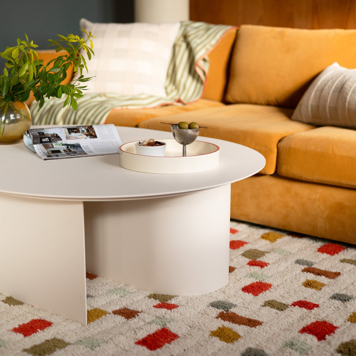 Pixel rug placed beneath a white coffee table in a living room, showing a plush cream surface with colorful geometric shapes